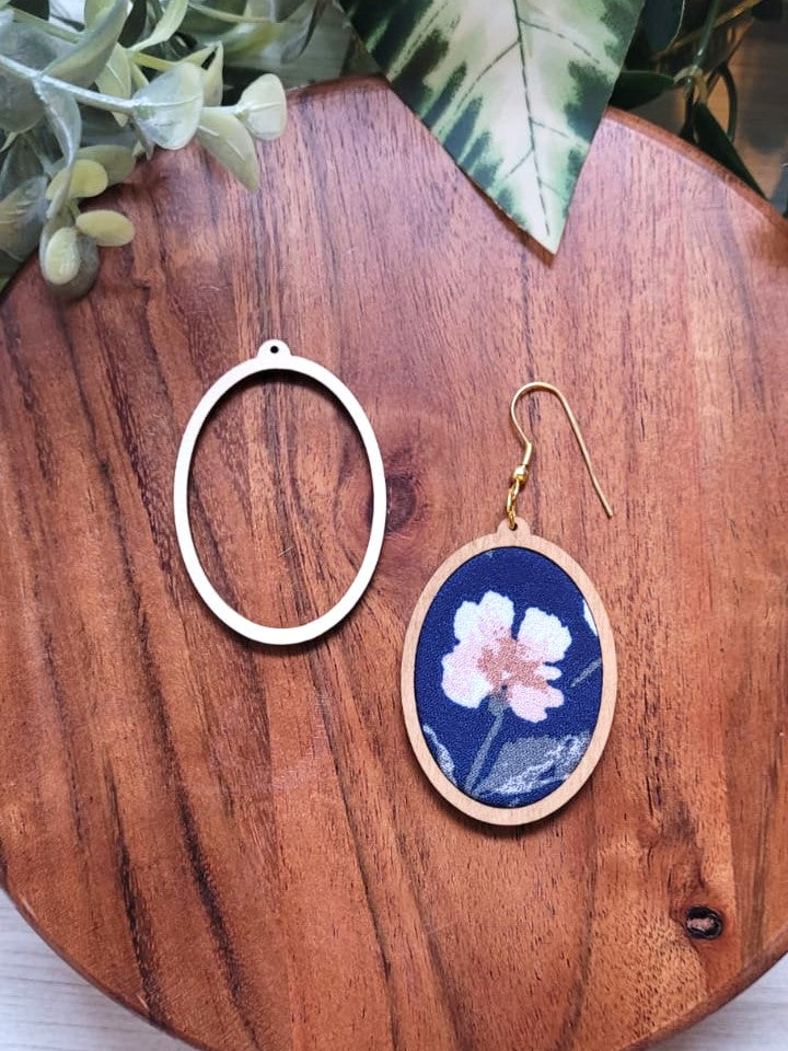 Image shows an oval shaped wooden frame and an earring made of fabric and the frame. The fabric is dark blue and has a pink flower on it.