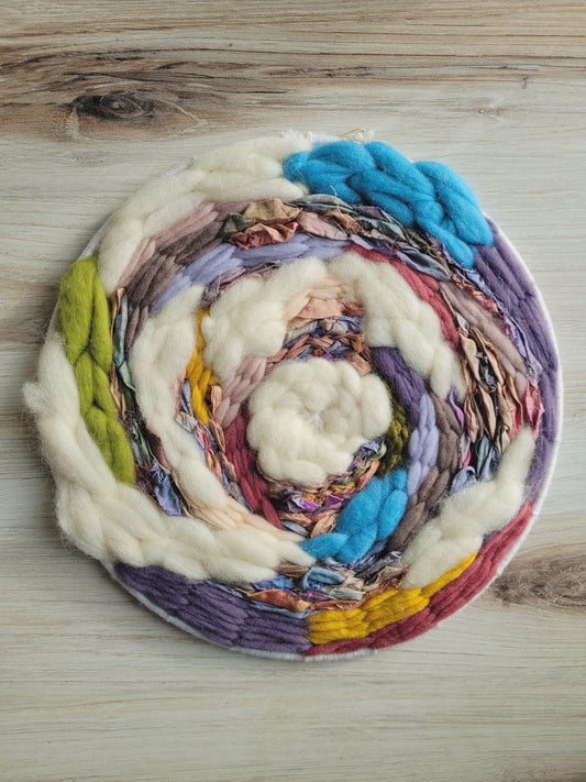 12" round weaving using white roving mixed with mauve, yellow, green, blue and purple roving as well as pastel rainbow ribbon. 