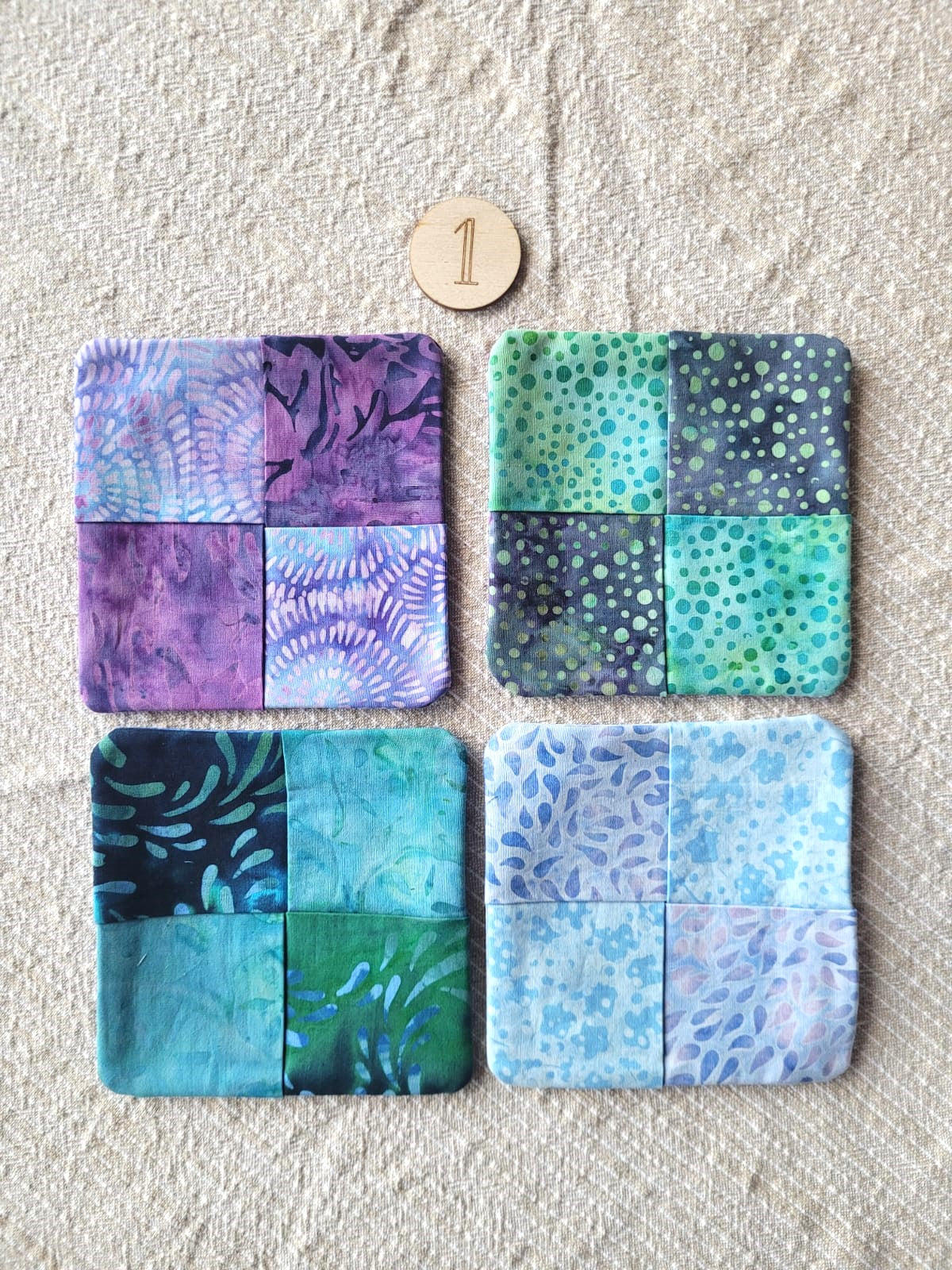 A set of four square fabric coasters made of batik fabrics in blues, purples, teals and greens. Each coaster is different prints. 