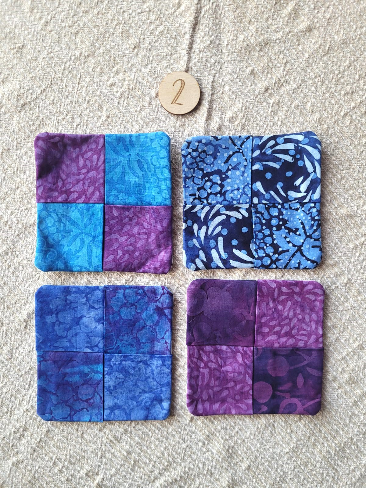 A set of four square fabric coasters made of batik fabrics in blues and purples. Each coaster is different prints. 