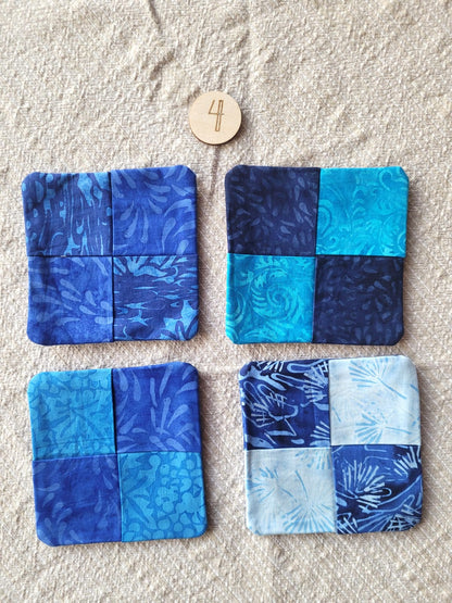 A set of four square fabric coasters made of batik fabrics in shades of blue. Each coaster is different prints. 