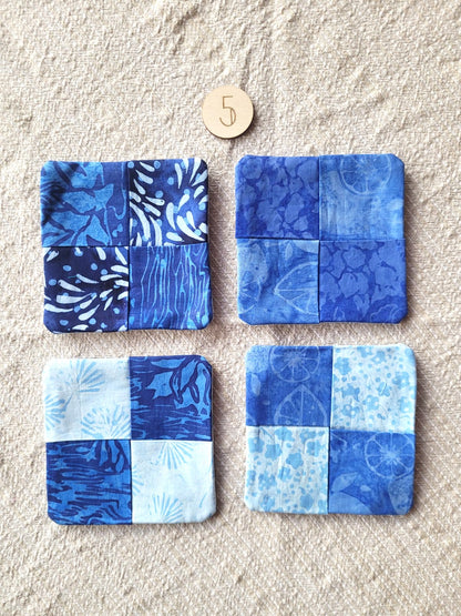 A set of four square fabric coasters made of batik fabrics in shades of blue. Each coaster is different prints. 