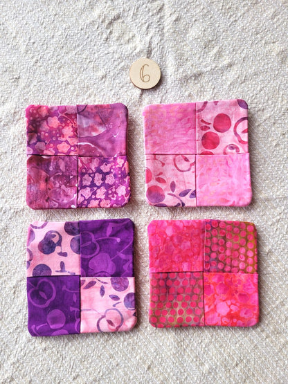 A set of four square fabric coasters made of batik fabrics in pinks, reds and purples. Each coaster is different prints. 