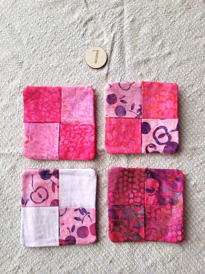 A set of four square fabric coasters made of batik fabrics in pinks, reds and purples. Each coaster is different prints. 