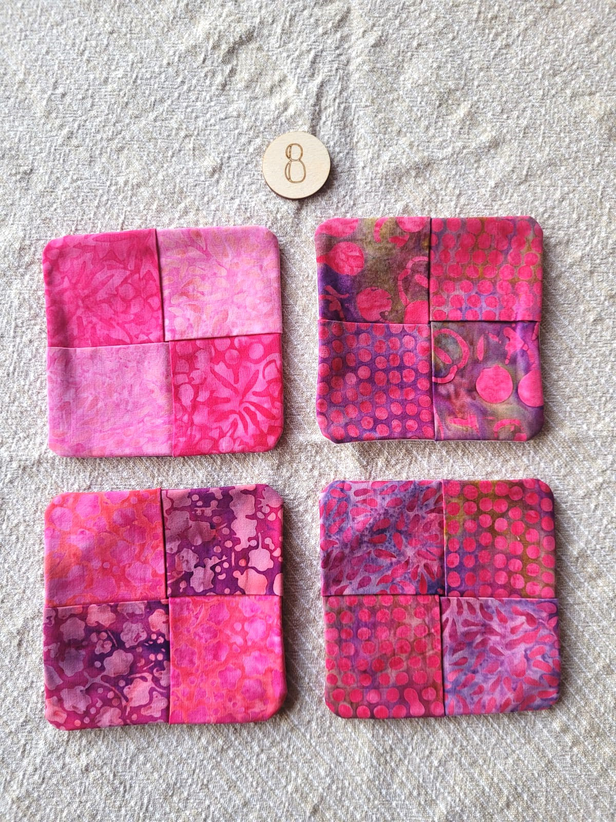 A set of four square fabric coasters made of batik fabrics in shades of pink. Each coaster is different prints. 